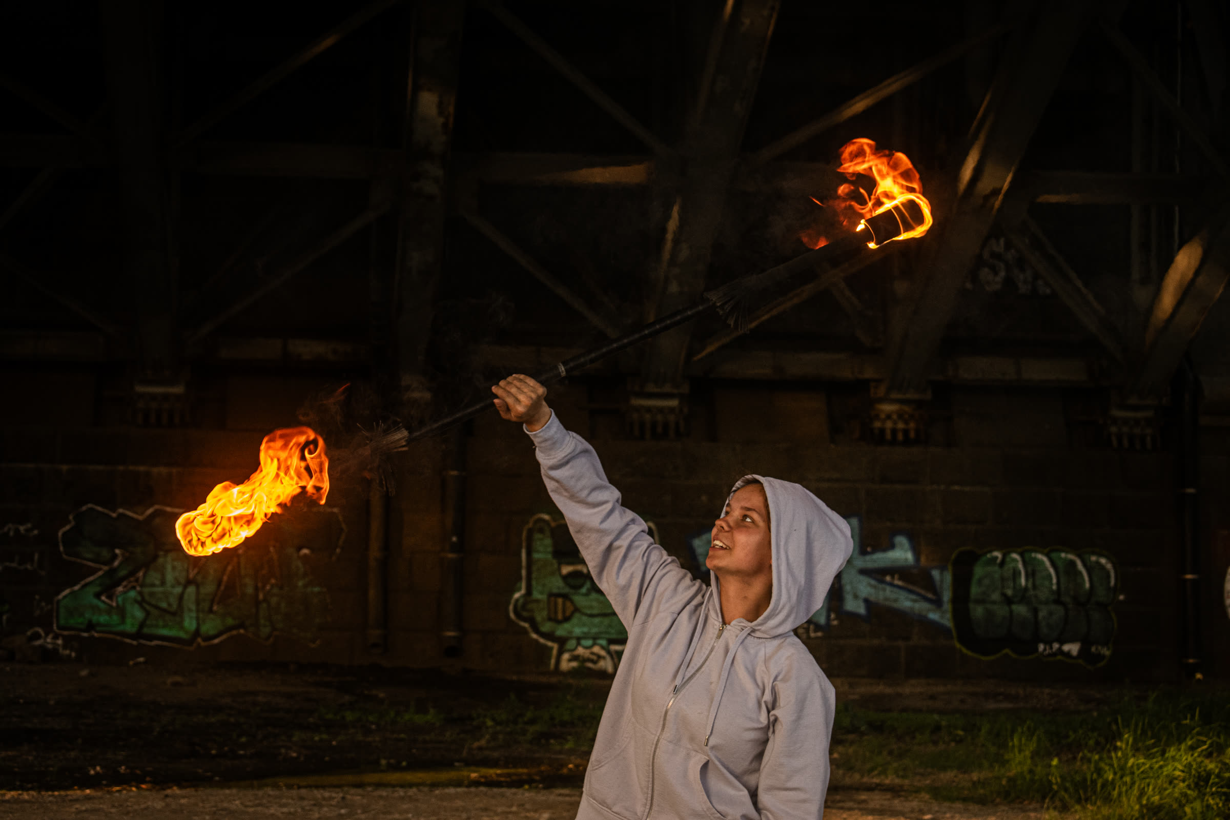 Dagmara unosi płonący kij przy murze z graffiti